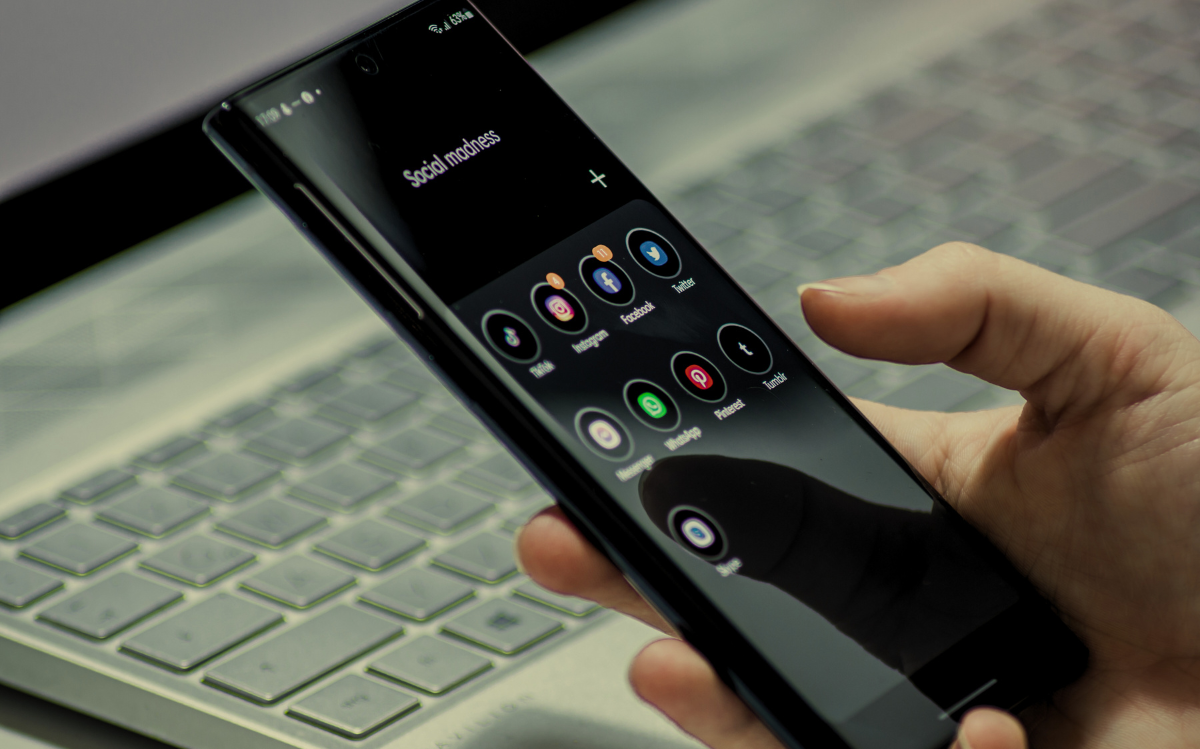 A person's hands holding a smartphone with various social media app icons displayed on the screen, suggesting the integration of mobile technology and digital platforms.