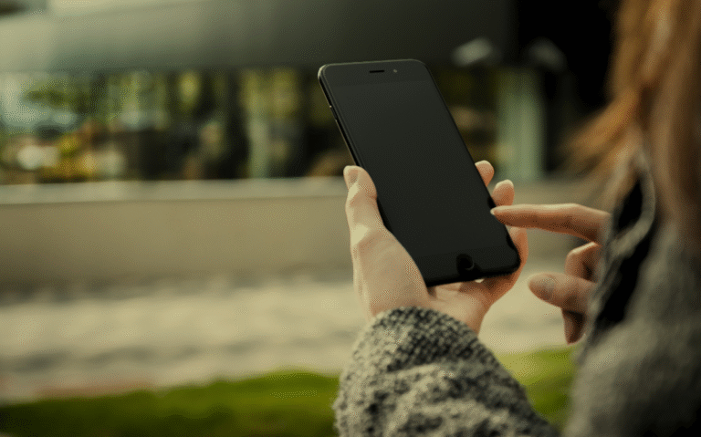 A person's hands holding a smartphone in an outdoor environment, suggesting the use of mobile devices to access information or communicate while in natural settings.