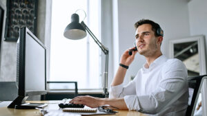 Customer service representative speaking on a headset while typing on a keyboard in a modern workspace.