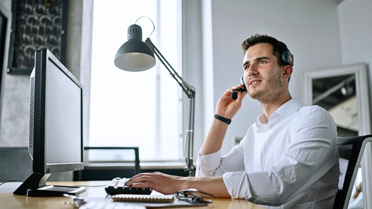 Customer service representative speaking on a headset while typing on a keyboard in a modern workspace.